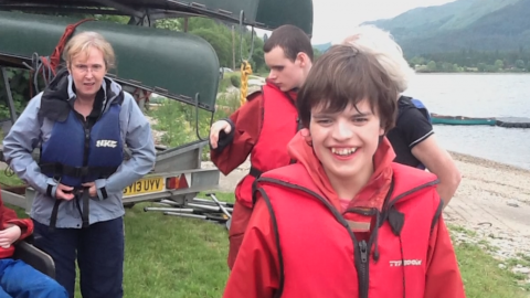 Pupils and teachers putting on life jackets beside a loch with canoes