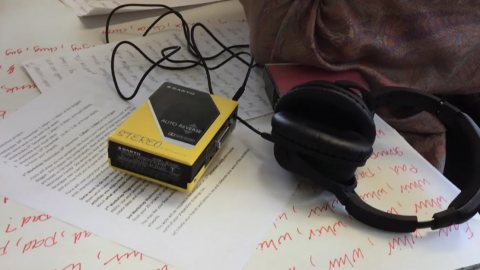 Personal stereo and headphones lying on a table on top of sheets of paper with illegible writing